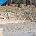Sits on the south slope of the Acropolis and is considered the birthplace of Western theater. The front row still preserves elaborately carved marble seats reserved for priests and civic leaders. The throne-like seat (right of center under the scaffolding) was reserved for the Priest of Dionysus Eleuthereus, the chief priest of the god Dionysus (the god of wine, festivals, and theater). The theatre is one of many features on the path up to the top of the Acropolis. (3112)
