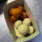 Loukoumades are Greek doughnut holes made from a simple yeast dough, deep-fried until golden, and typically drizzled with honey syrup and sprinkled with cinnamon. They are a popular dessert in Greece, often enjoyed at festivals and family gatherings. The yellow-greenish ones are covered with a pistachio cream sauce. (3982)